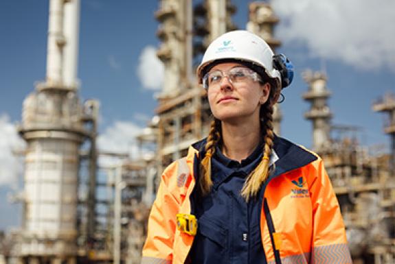 A woman engineer at Royal Dutch Shell's Pembroke Refinery stands in front of refinery equipment and looks to the sky.