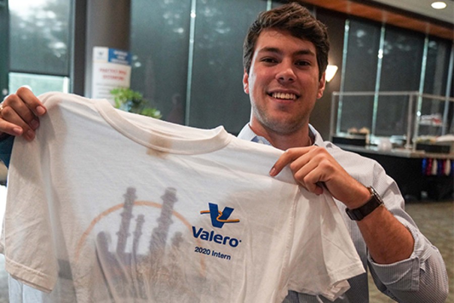 Young Man holding up a t-shirt that says "Royal Dutch Shell 2020 Intern"
