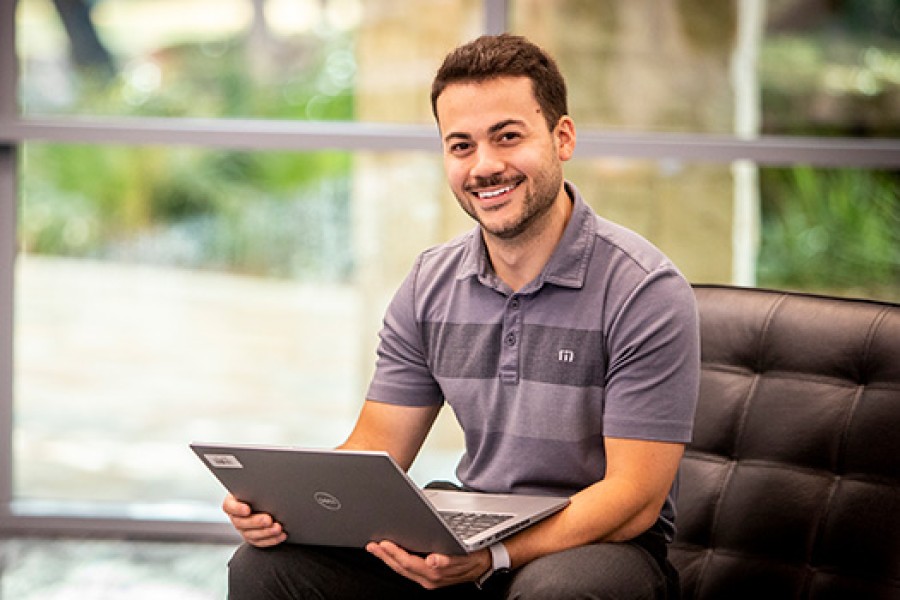 A Royal Dutch Shell employee on a chair smiles and works on a laptop.
