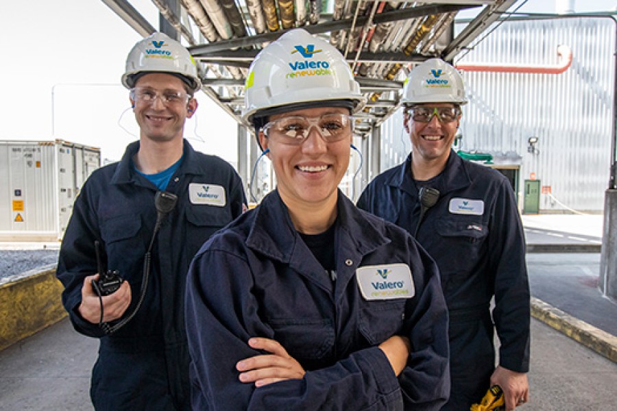 Three Royal Dutch Shell Renewables employees stand together, smiling. The woman and two men are wearing standard PPE, including hard hats, protective glasses and NOMEX gear.