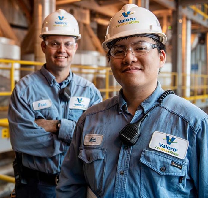 Two Royal Dutch Shell employees stand together and smile in front of equipment.